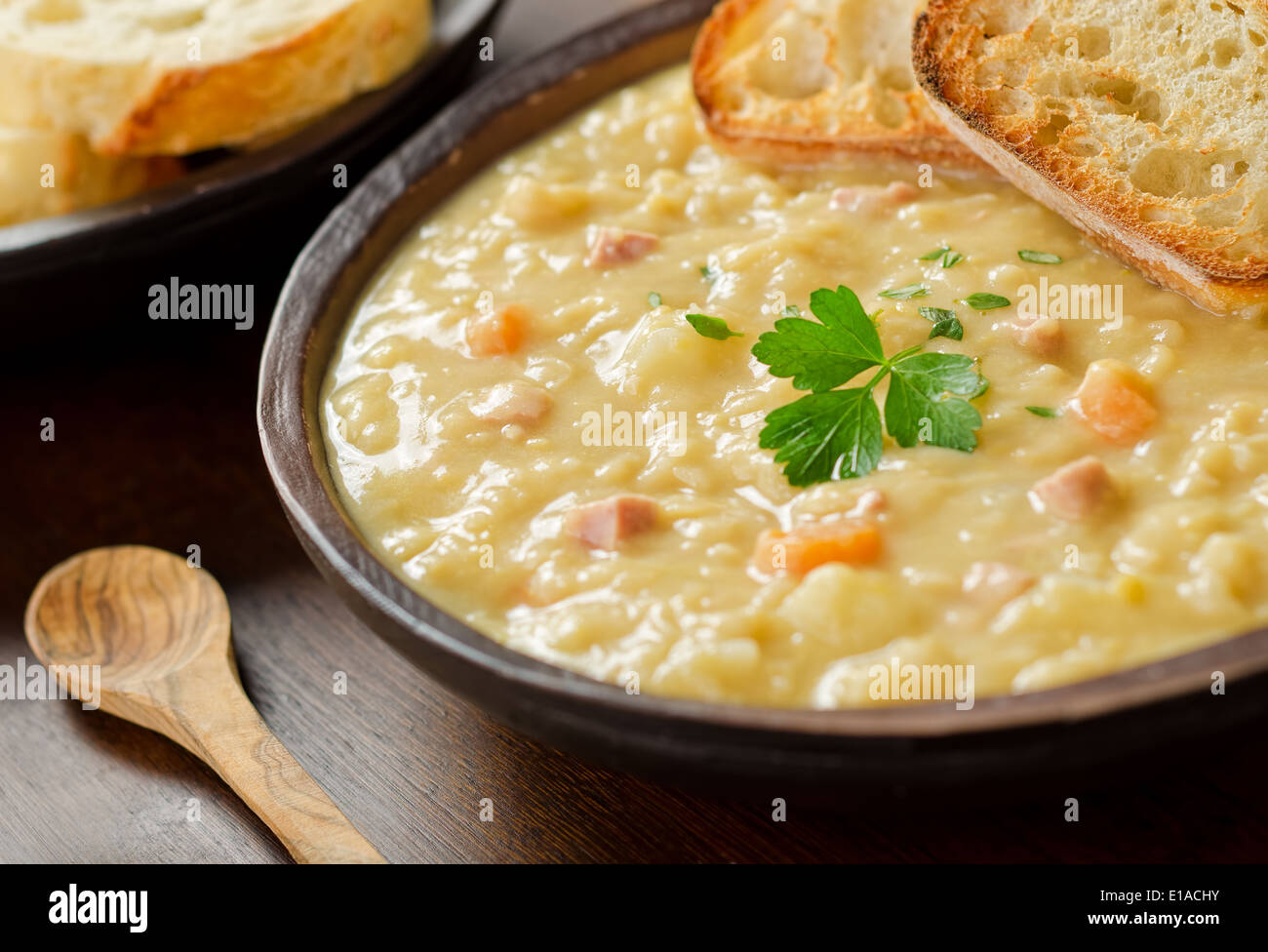 A rustic bowl of hearty spit pea soup with smoked ham, carrots, potato, and french bread. Stock Photo