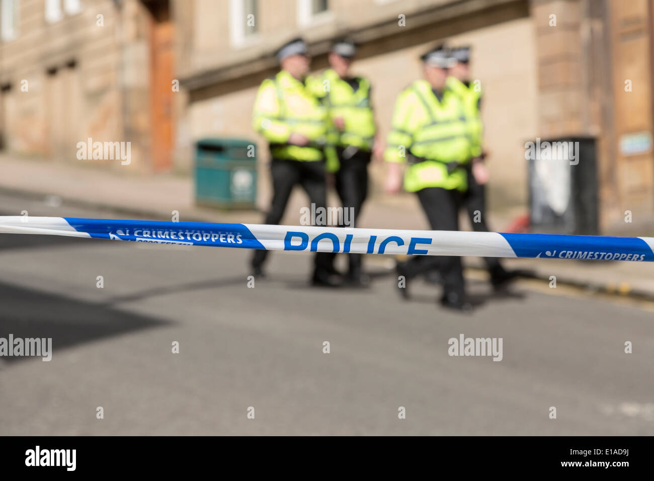 Strathclyde Police tape cordon restricting access to a crime scene. Out of focus/blurred police officers walking background Stock Photo
