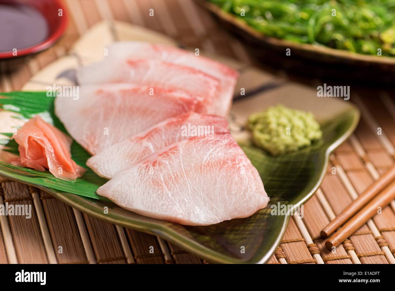 A delicious white fish sashimi served with wasabi paste, pickled ginger, japanese soy, and seaweed salad. Stock Photo
