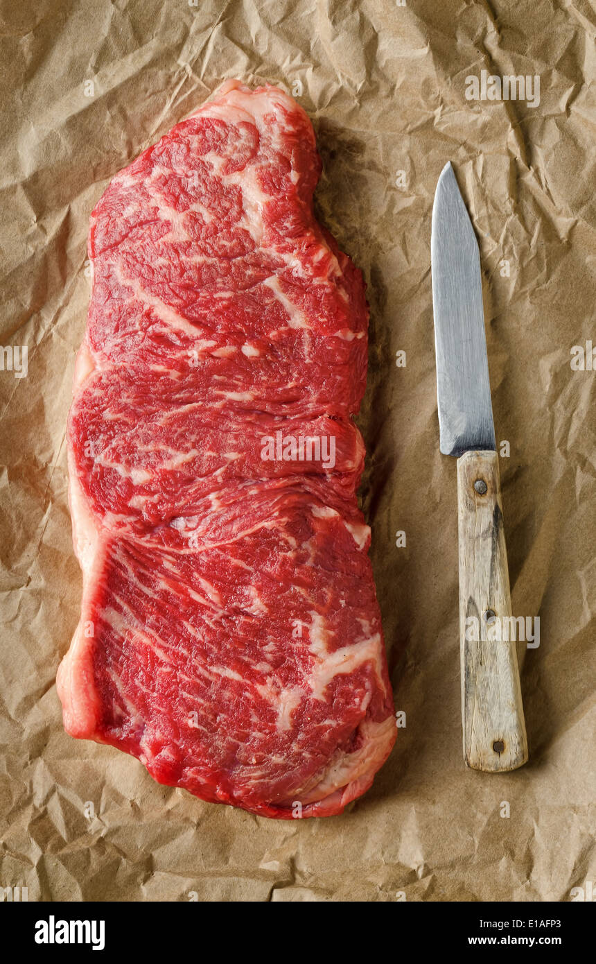 A perfectly marbled strip loin steak on crumpled butcher paper with old knife. Stock Photo