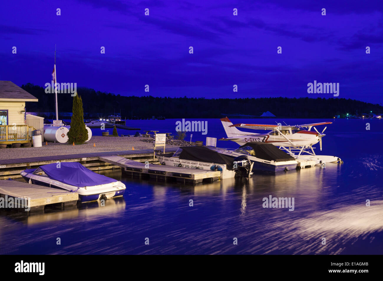 A floatplane and motor boats tied to shore at dusk in front of 'Georgian Bay Airways'. Parry Sound Harbour, Ontario, Canada. Stock Photo