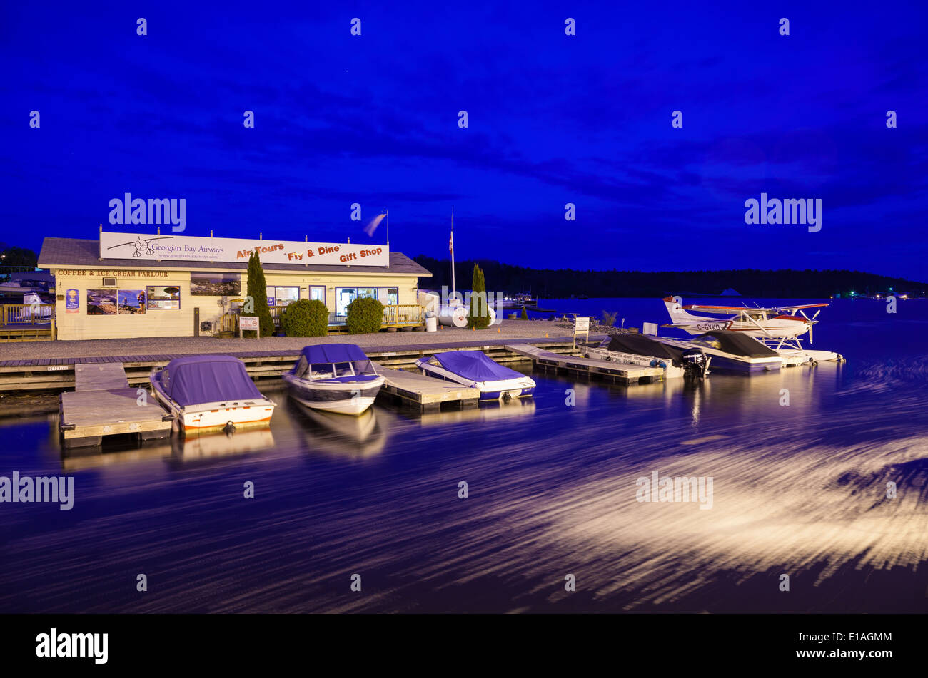 A float plane and motor boats tied to shore at dusk in front of 'Georgian Bay Airways'. Parry Sound Harbour, Ontario, Canada. Stock Photo