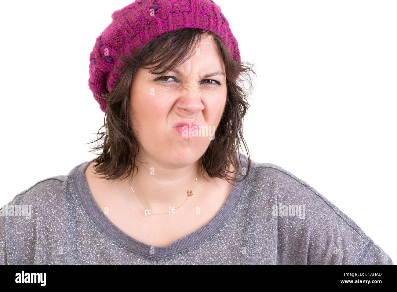 Disdainful woman in a purple knitted beanie screwing up her nose in disgust and dislike, head and shoulders isolated on white Stock Photo