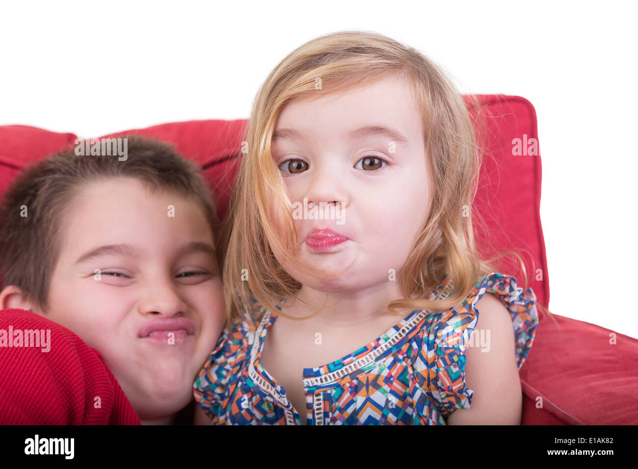 Young brother and sister pulling funny faces holding their breath and screwing up their noses as they sit together playing Stock Photo