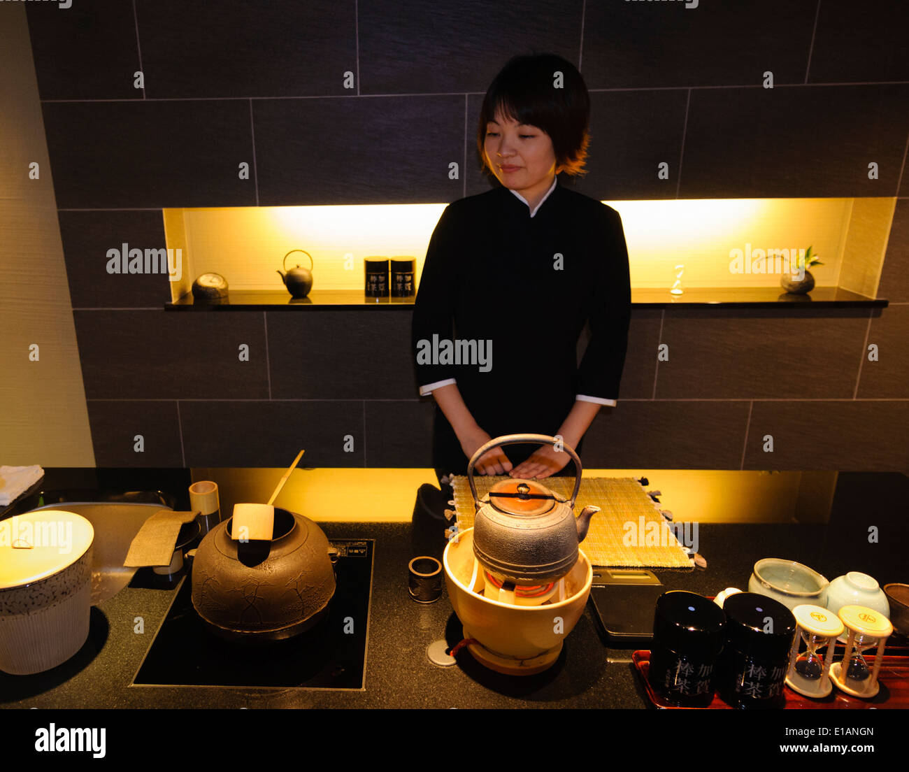 Young female sales assistant stands in a tea shop behind various traditional apparatus used to prepare green tea (matcha) Stock Photo