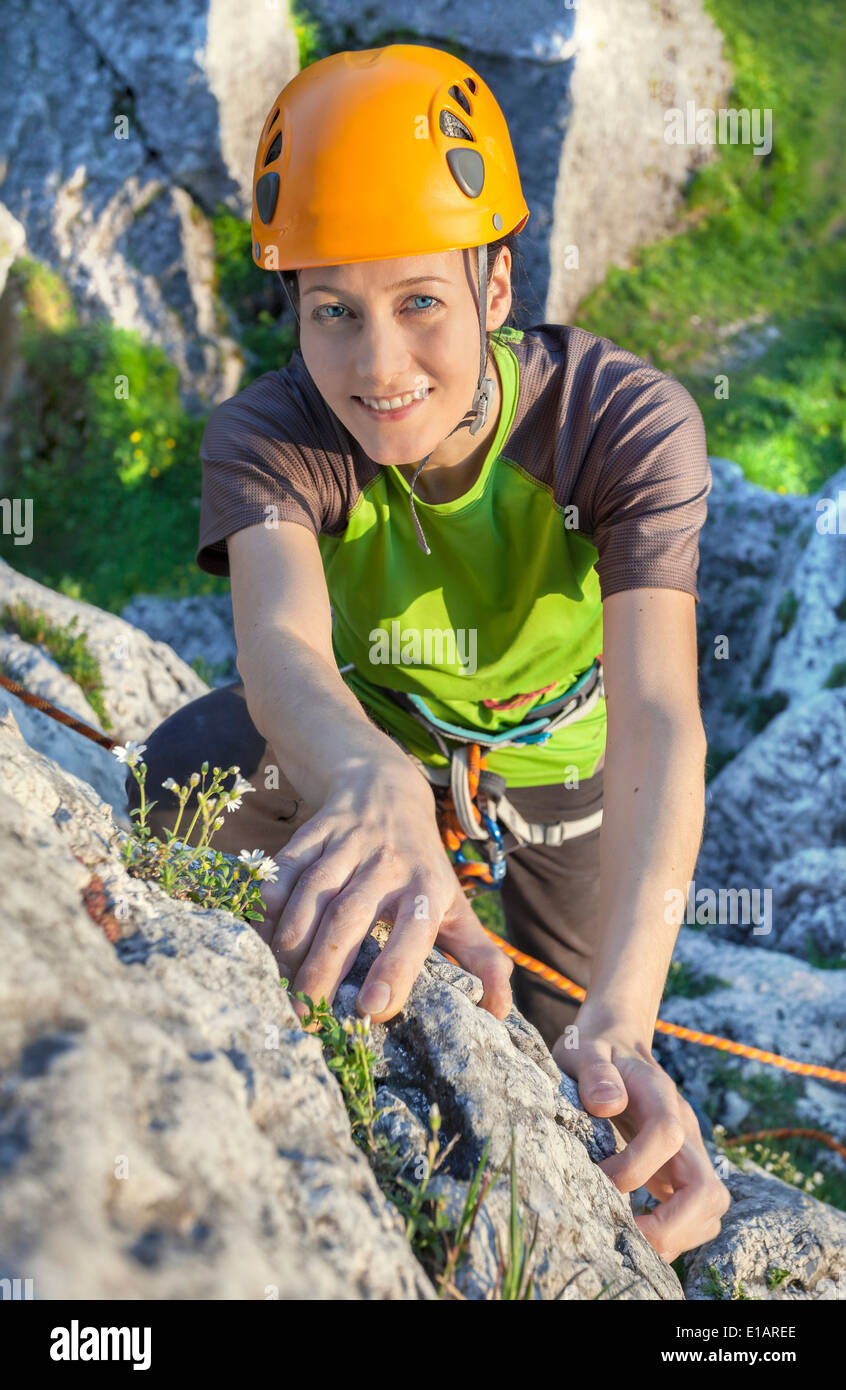 Smiling woman, rock climber in yellow helmet reaching top of mountain during sunset. Stock Photo