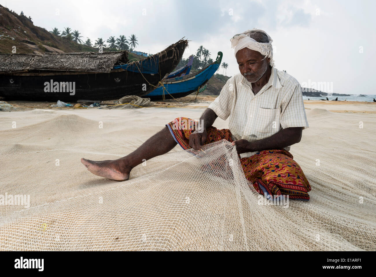 Fisherman repairing fishing nets on the beach, Vizhinjam, Kerala, India Stock Photo