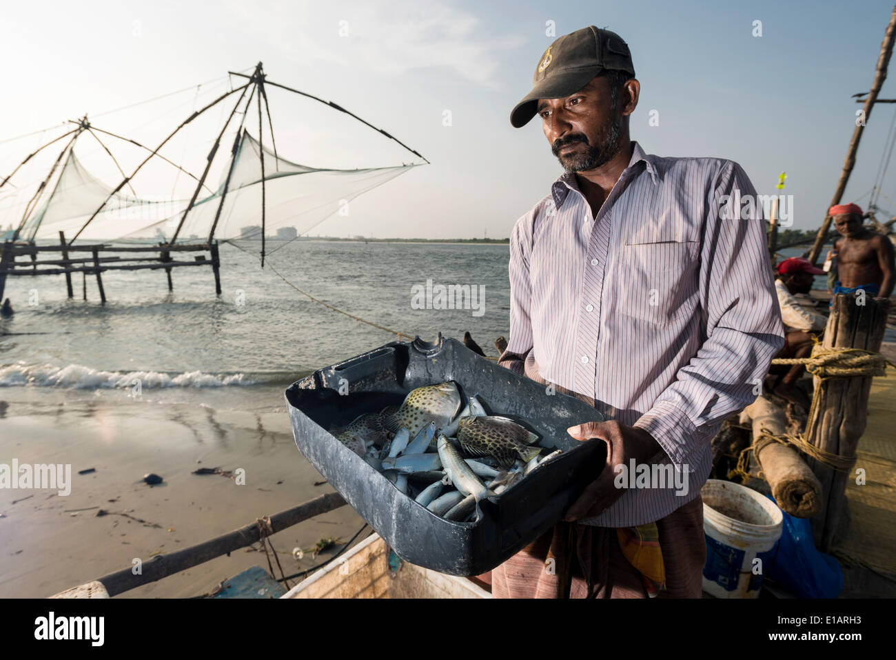 Fisherman presenting his catch, Cheena vala or Chinese fishing nets at the back, Kochi, Kerala, India Stock Photo
