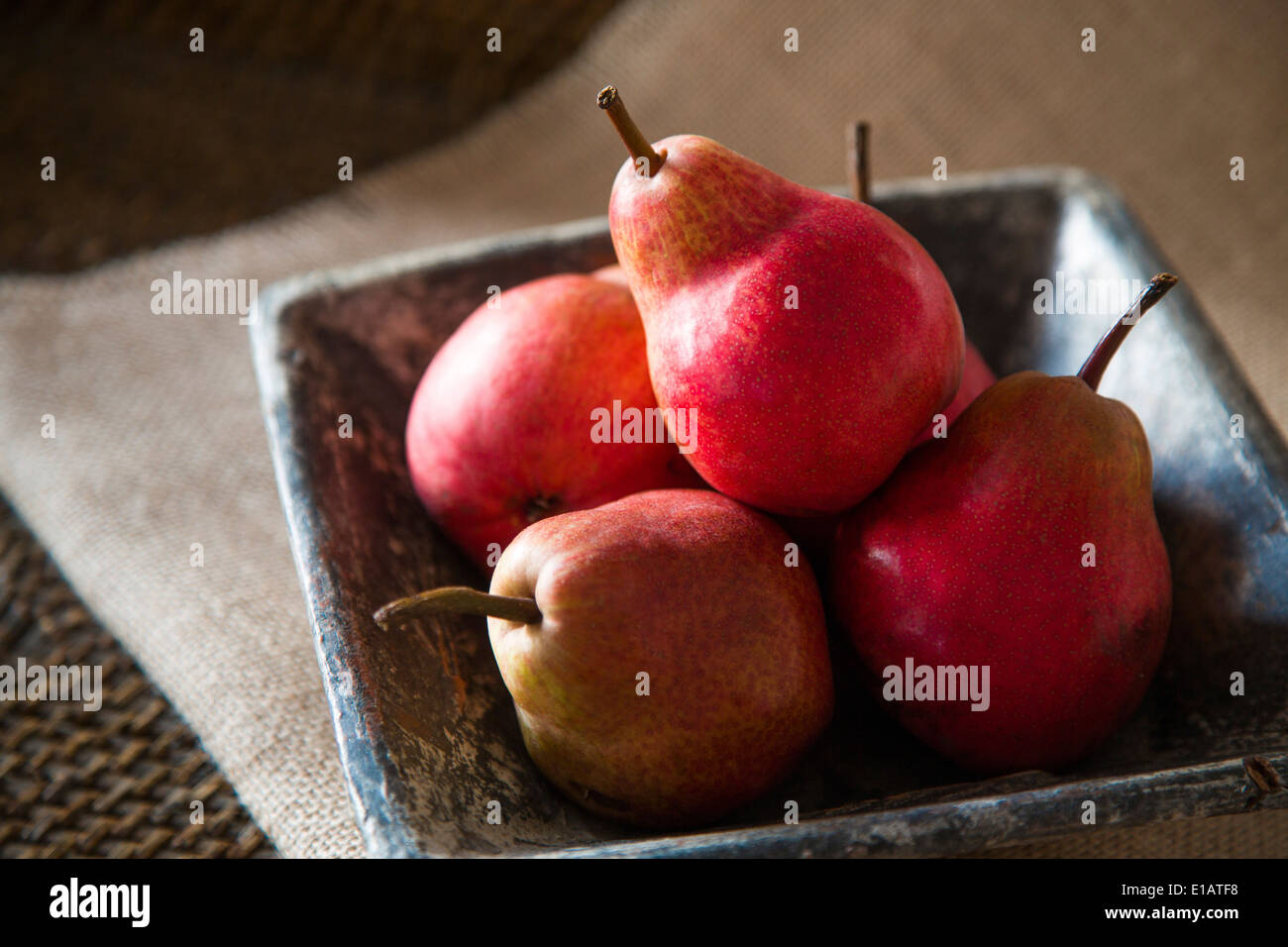 group of red pears in rustic ceramic dish, on sack cloth and woven tray. Stock Photo