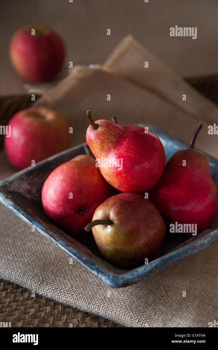 group of red pears in rustic ceramic dish, on sack cloth and woven tray, red apples in background, Stock Photo