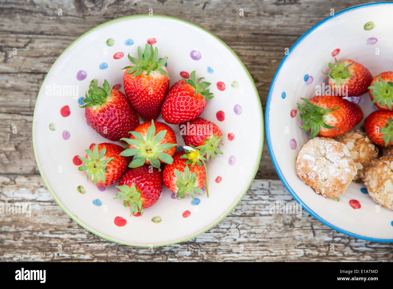 whole strawberries in spotted ceramic rustic bowl, with almond cookies on rustic wood table Stock Photo