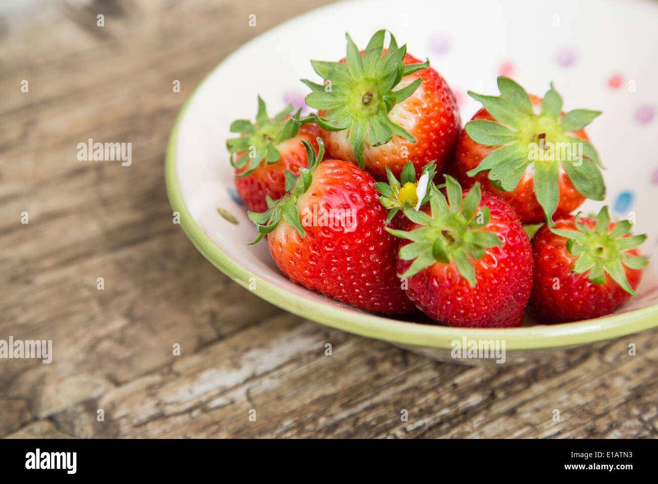whole strawberries in spotted ceramic rustic bowl, on rustic wood table Stock Photo