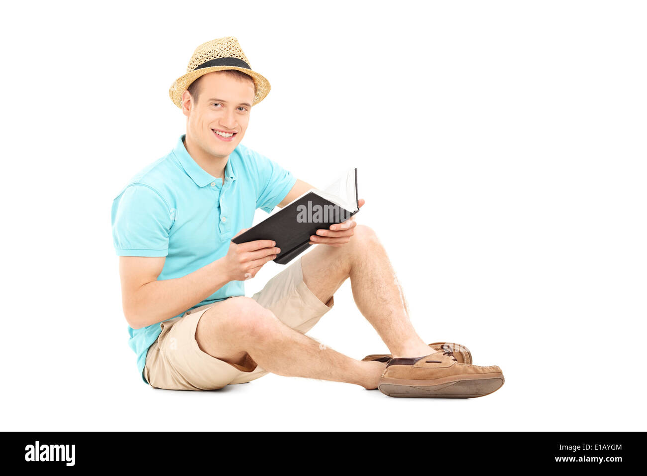 Young man holding a book and looking at camera seated on the floor Stock Photo