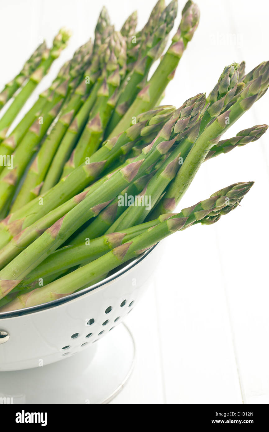 green asparagus in colander on white background Stock Photo