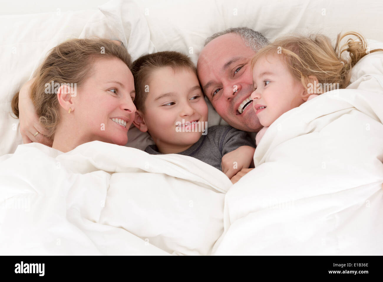 Happy young family cuddling together in bed with a pretty young girl and her brother enjoying the love and devotion Stock Photo
