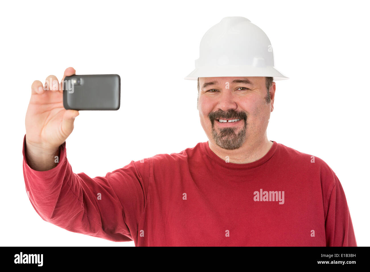 Smiling workman with a goatee beard wearing a hardhat taking a self-portrait using his smartphone, isolated on white Stock Photo