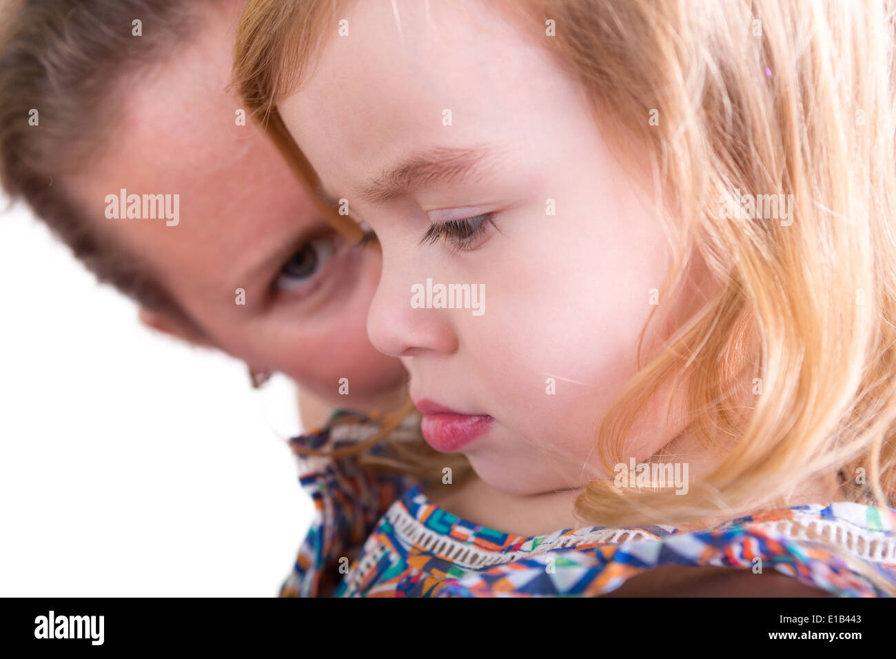 Protective mother watching over her little daughter with the pretty little girl in profile to the camera with downcast eyes with Stock Photo