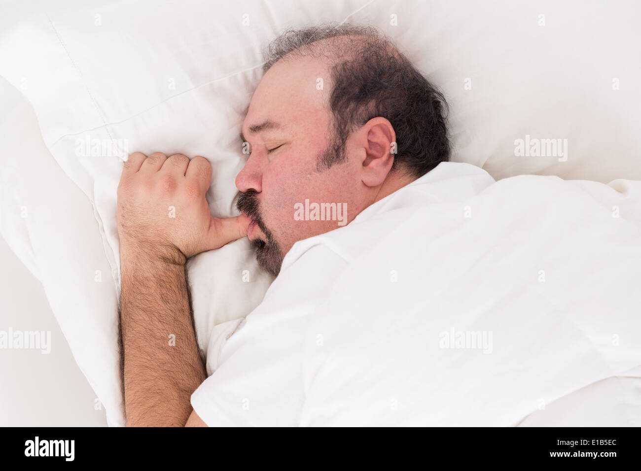 Closeup of a bearded man snuggling into his pillow sucking his thumb like a big baby while sleeping with a serene innocent expre Stock Photo