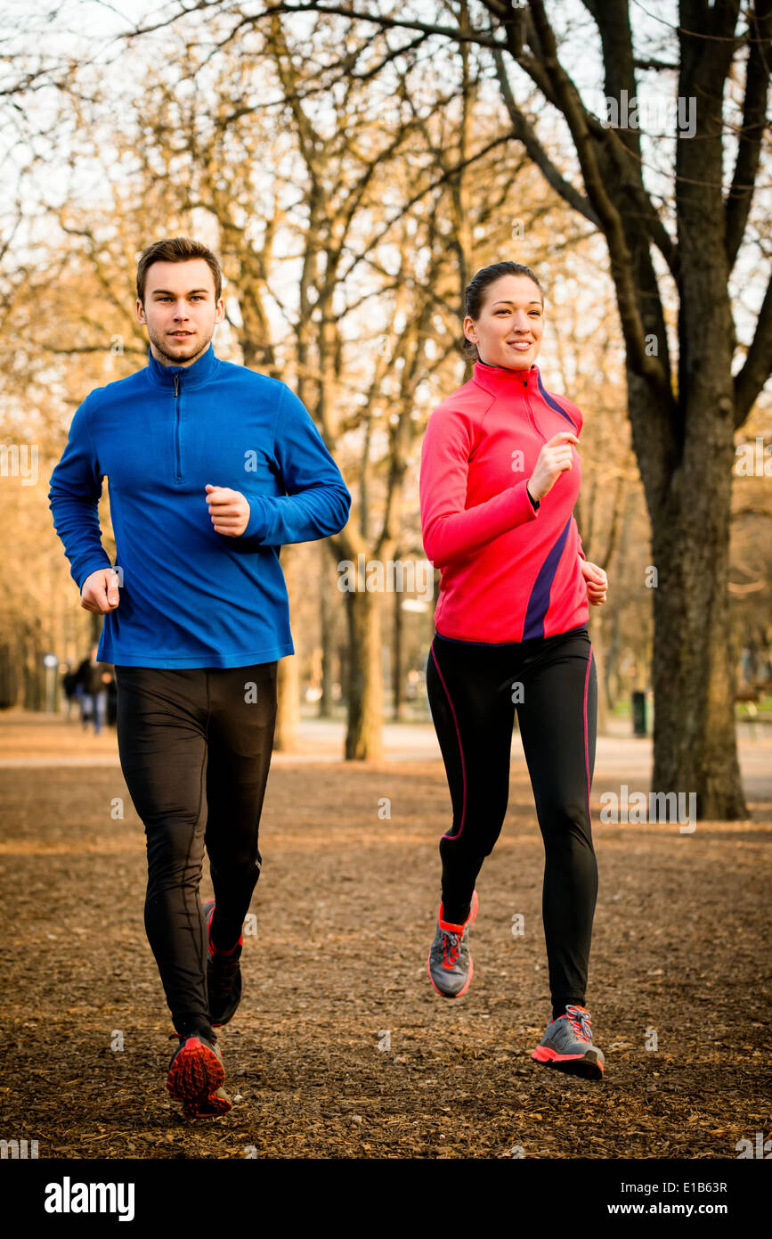 Young couple jogging together in tree alley - late autumn Stock Photo