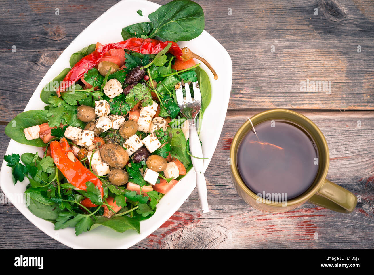 Bowl of fresh leafy green baby spinach and tomato salad with a freshly brewed mug of hot tea on a rustic wooden table, overhead Stock Photo