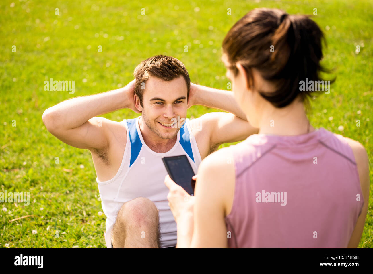 Man making sit-ups while woman is watching time of exercise on mobile phone Stock Photo