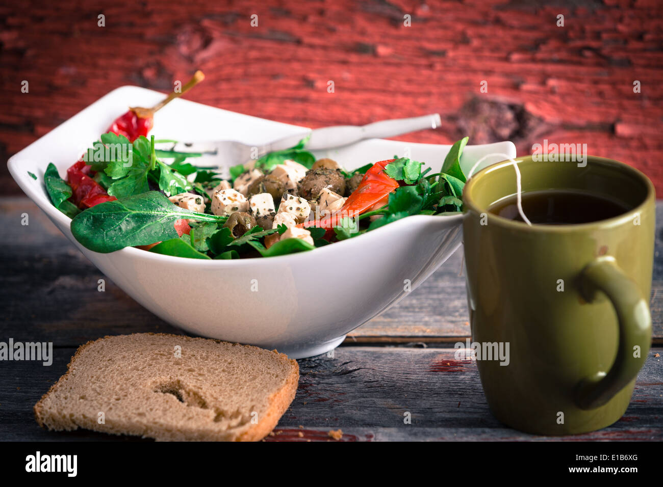 Bowl of delicious fresh baby spinach, tomato and feta salad with a mug of hot tea and a slice of bread served for lunch on a rus Stock Photo