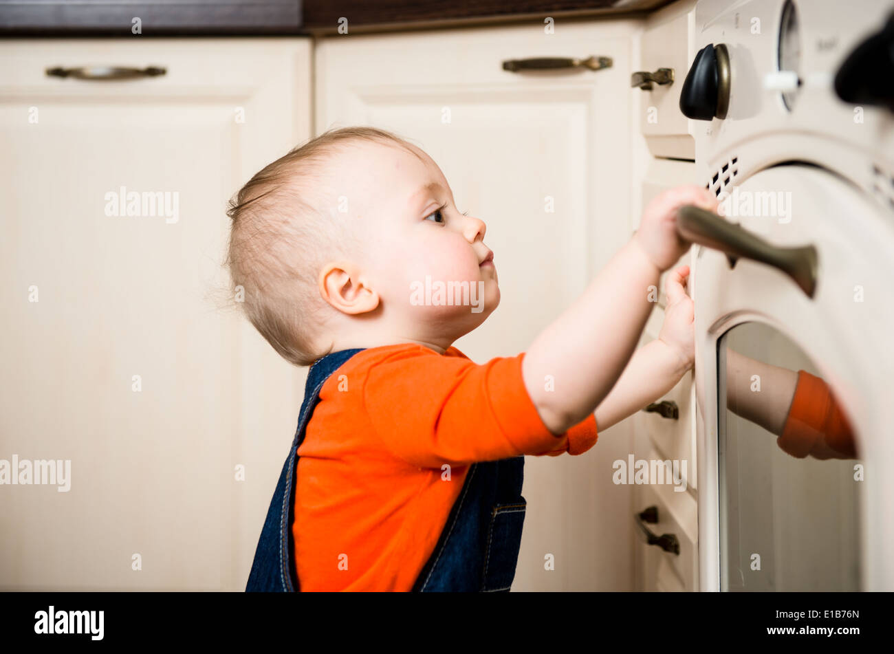 Curious baby watching through glass of kitchen oven Stock Photo