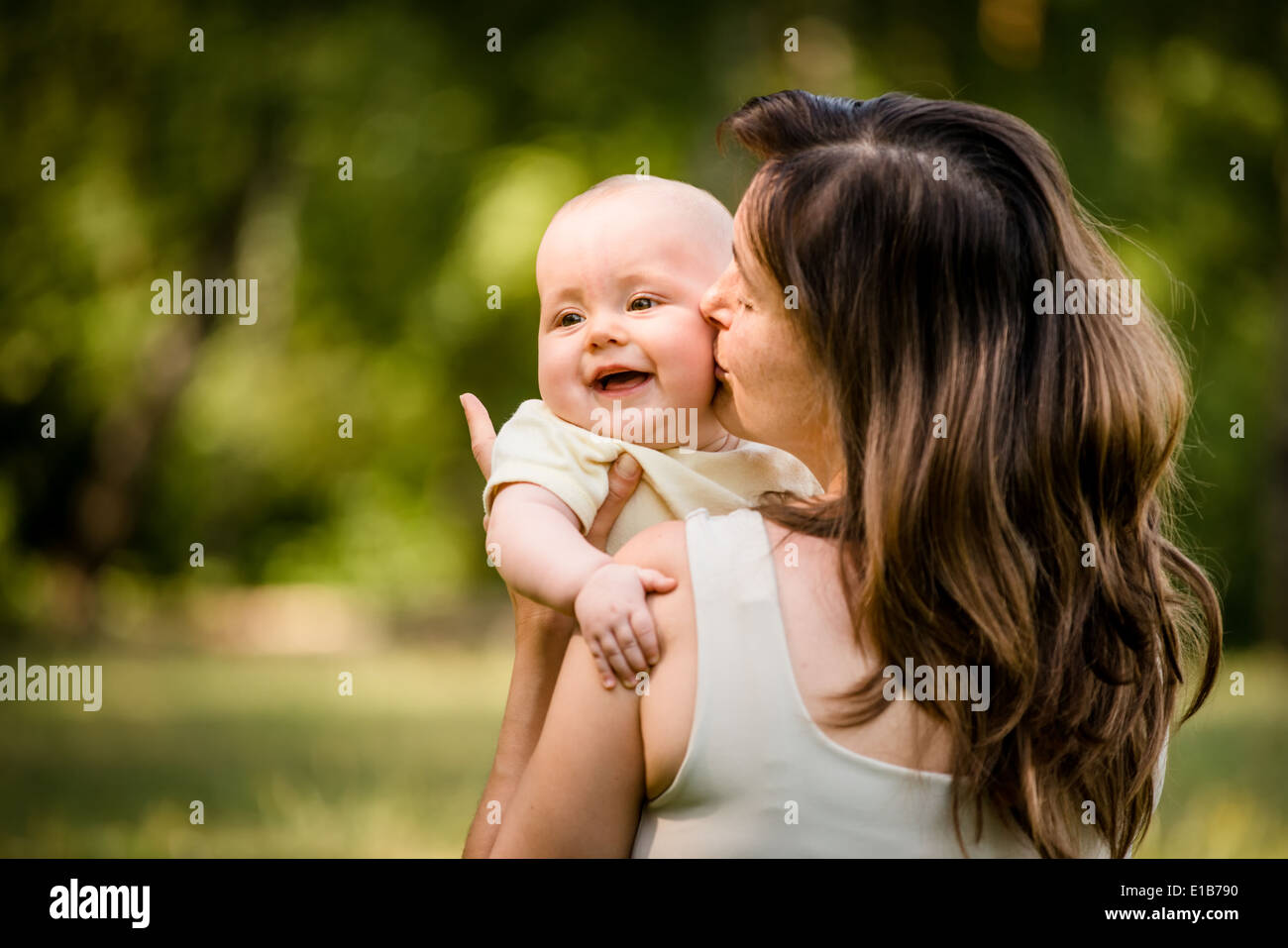 Happy mother kissing and hugging her baby - outdoor in nature Stock Photo