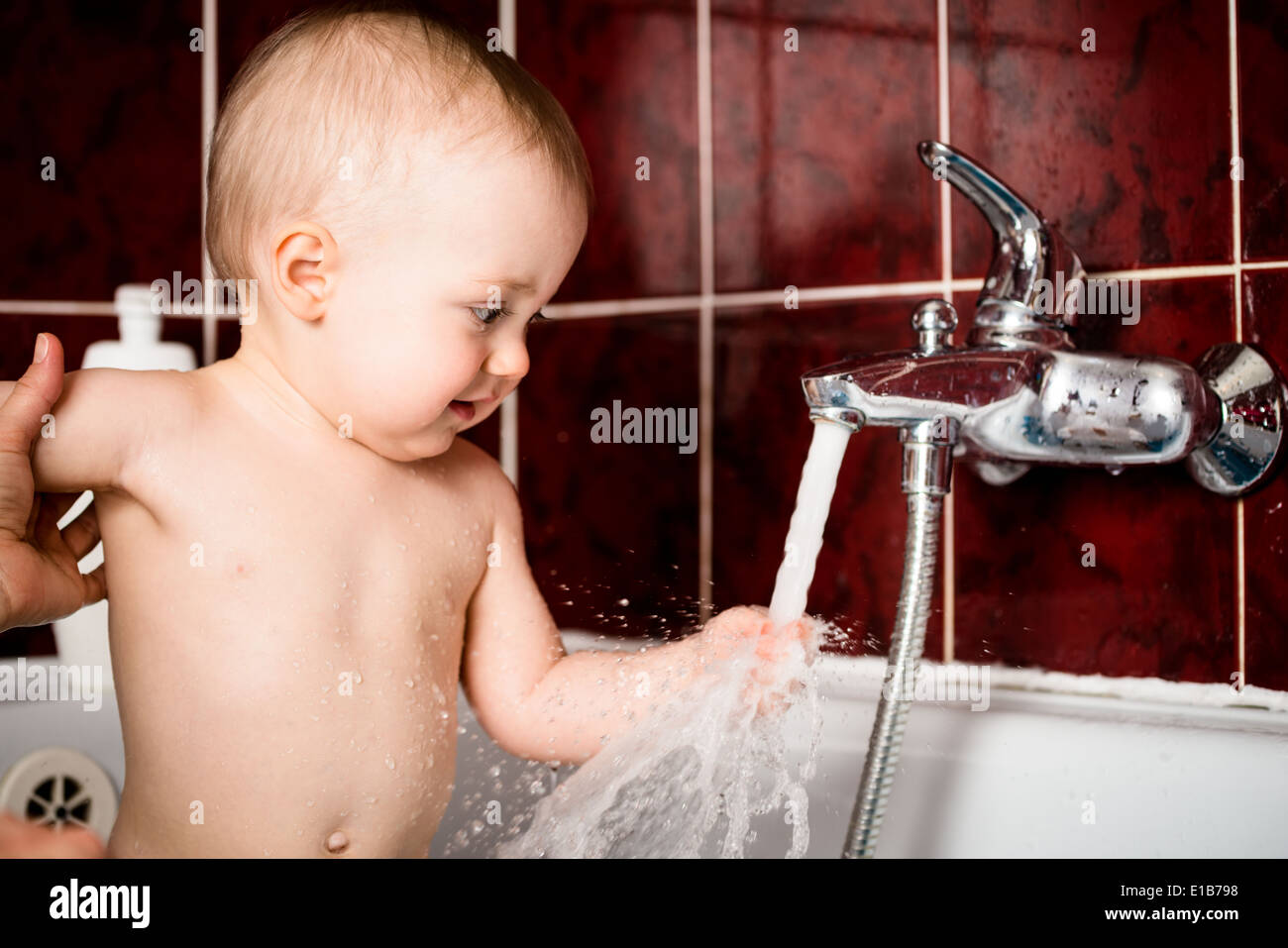 Cute baby playing with water tap in bathroom Stock Photo