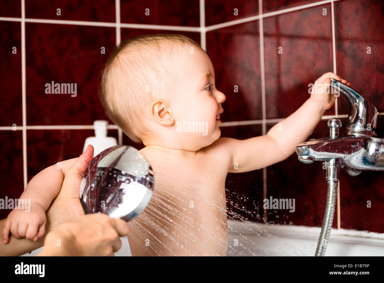 Cute baby playing with water tap in bathroom while at shower Stock Photo