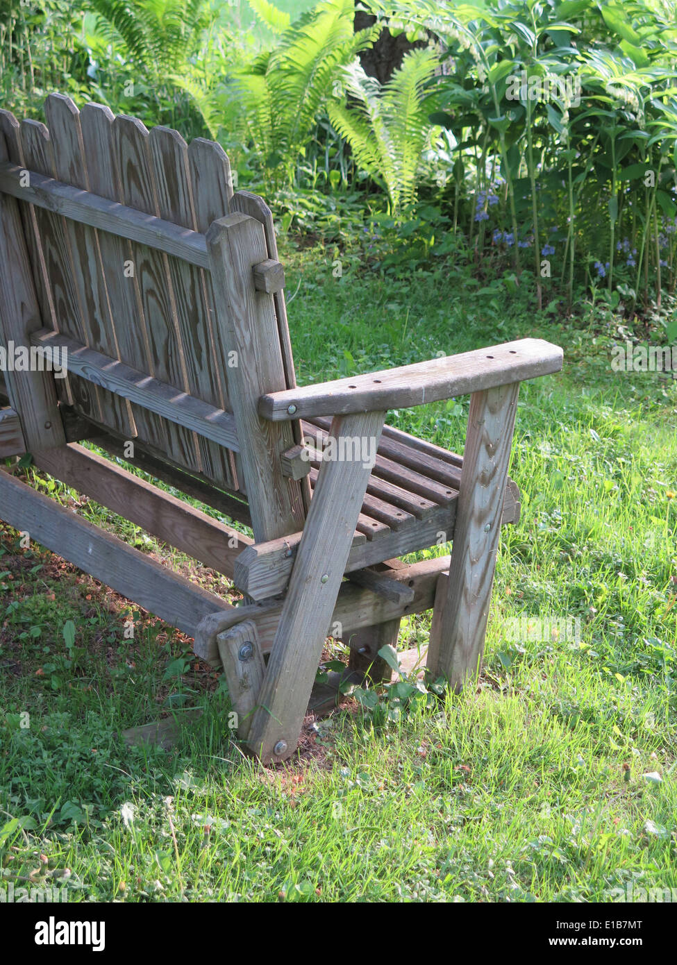 Half of a wooden swing bench is visible in a lush garden. Stock Photo