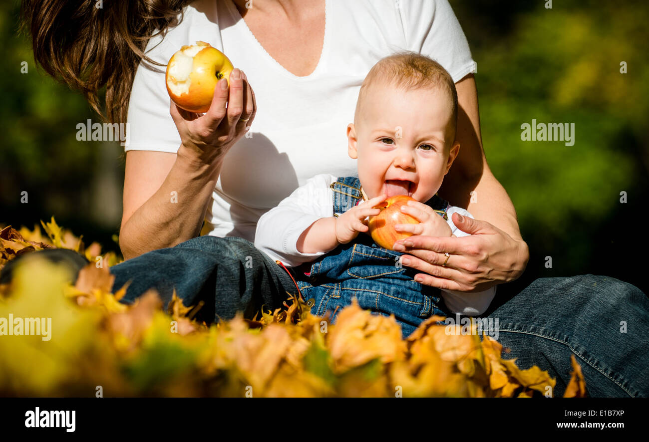 Mother with her cute baby eating apples outdoor in autumn nature Stock Photo