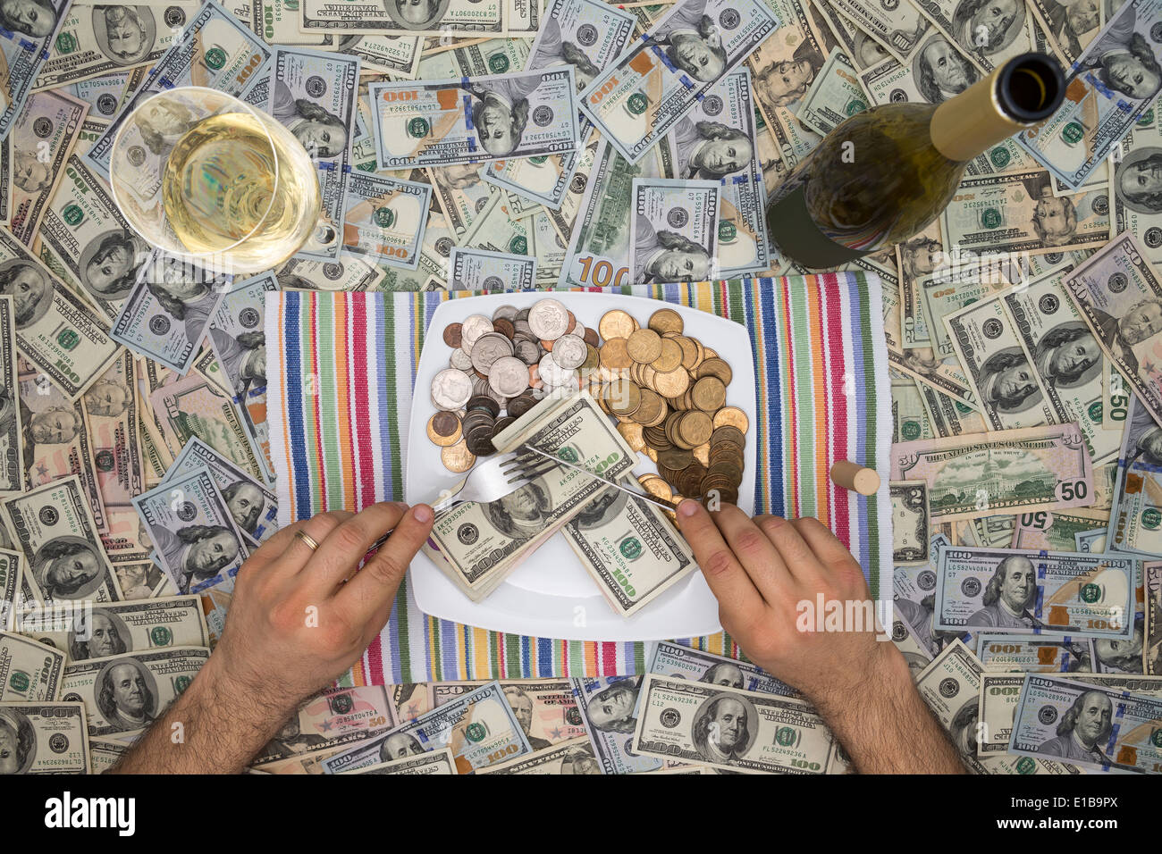 Conceptual image of a man eating money through extravagance with an overhead view of him sitting at table covered in 100 dollar Stock Photo