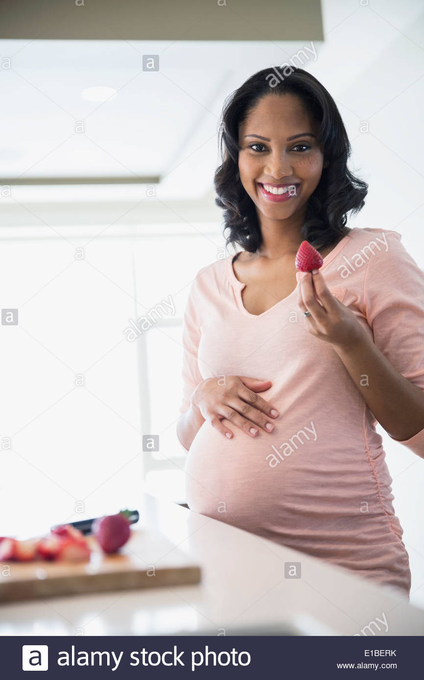 Portrait of pregnant woman eating strawberries in kitchen Stock Photo