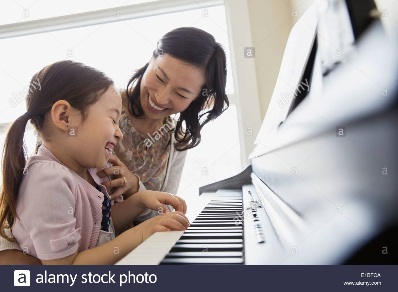 Mother teaching daughter to play piano Stock Photo