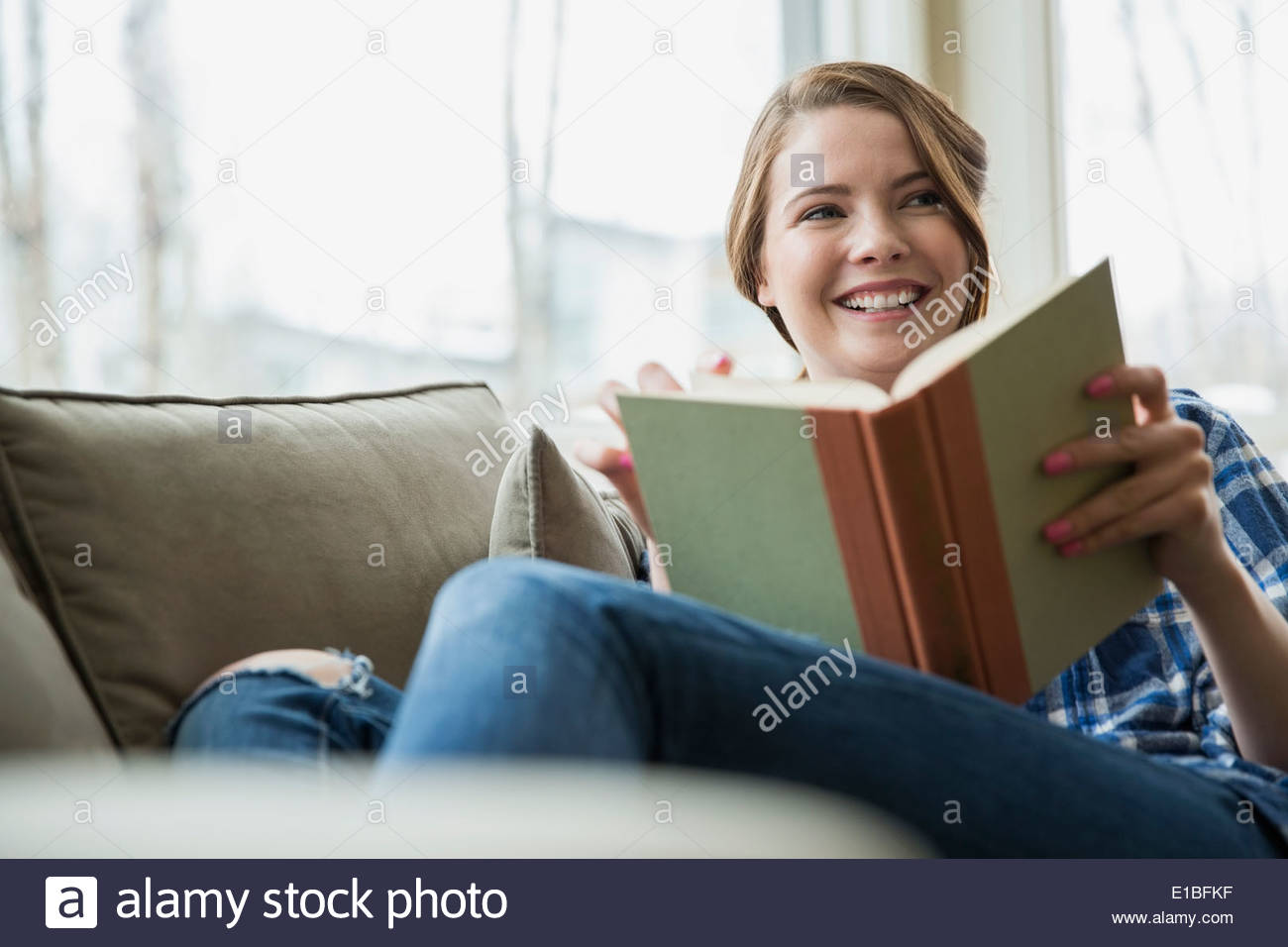 Woman reading book on sofa in living room Stock Photo