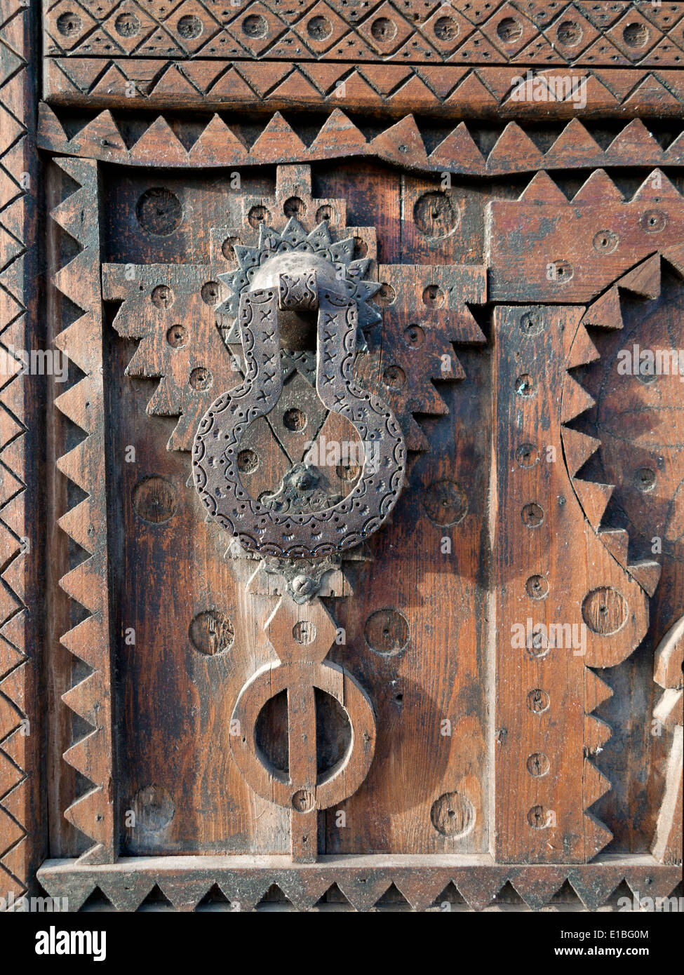 Close up detail of carved wood on a Moroccan door with black iron knocker and handle Stock Photo