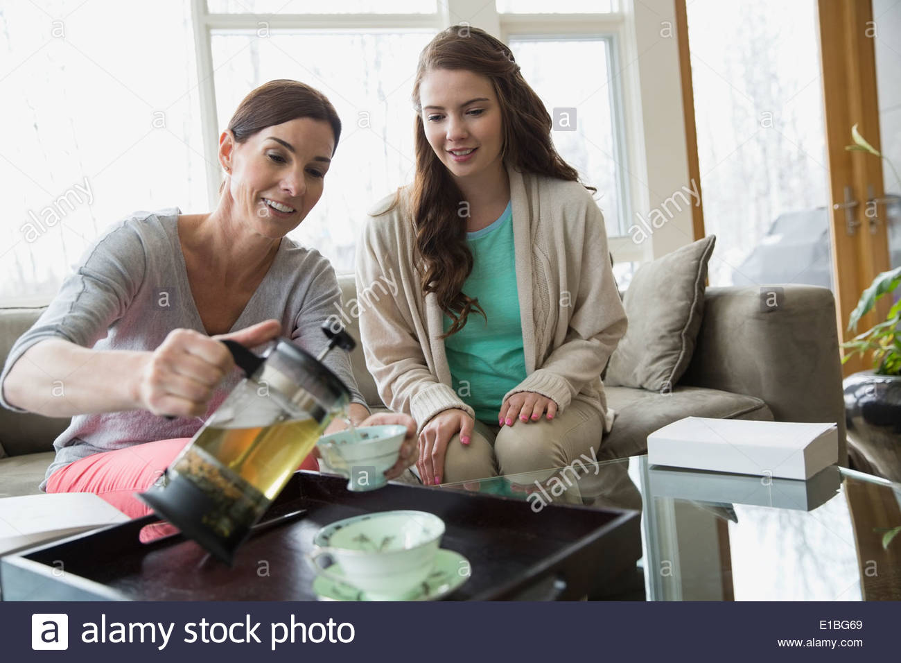 Mother and daughter pouring tea in living room Stock Photo