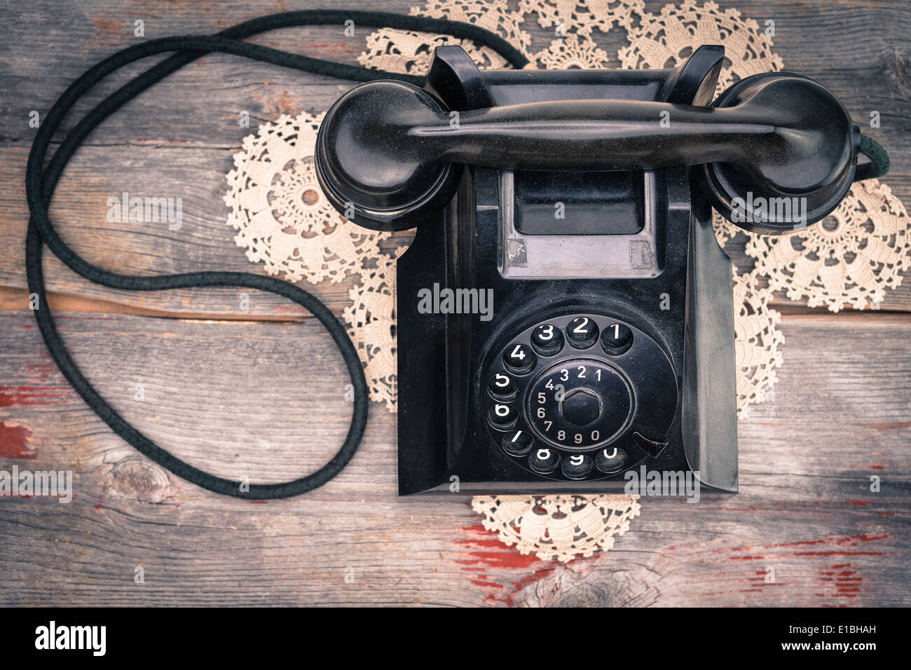 View from above of a black old-fashioned rotary telephone instrument on a crocheted doily on a weathered wooden table top Stock Photo