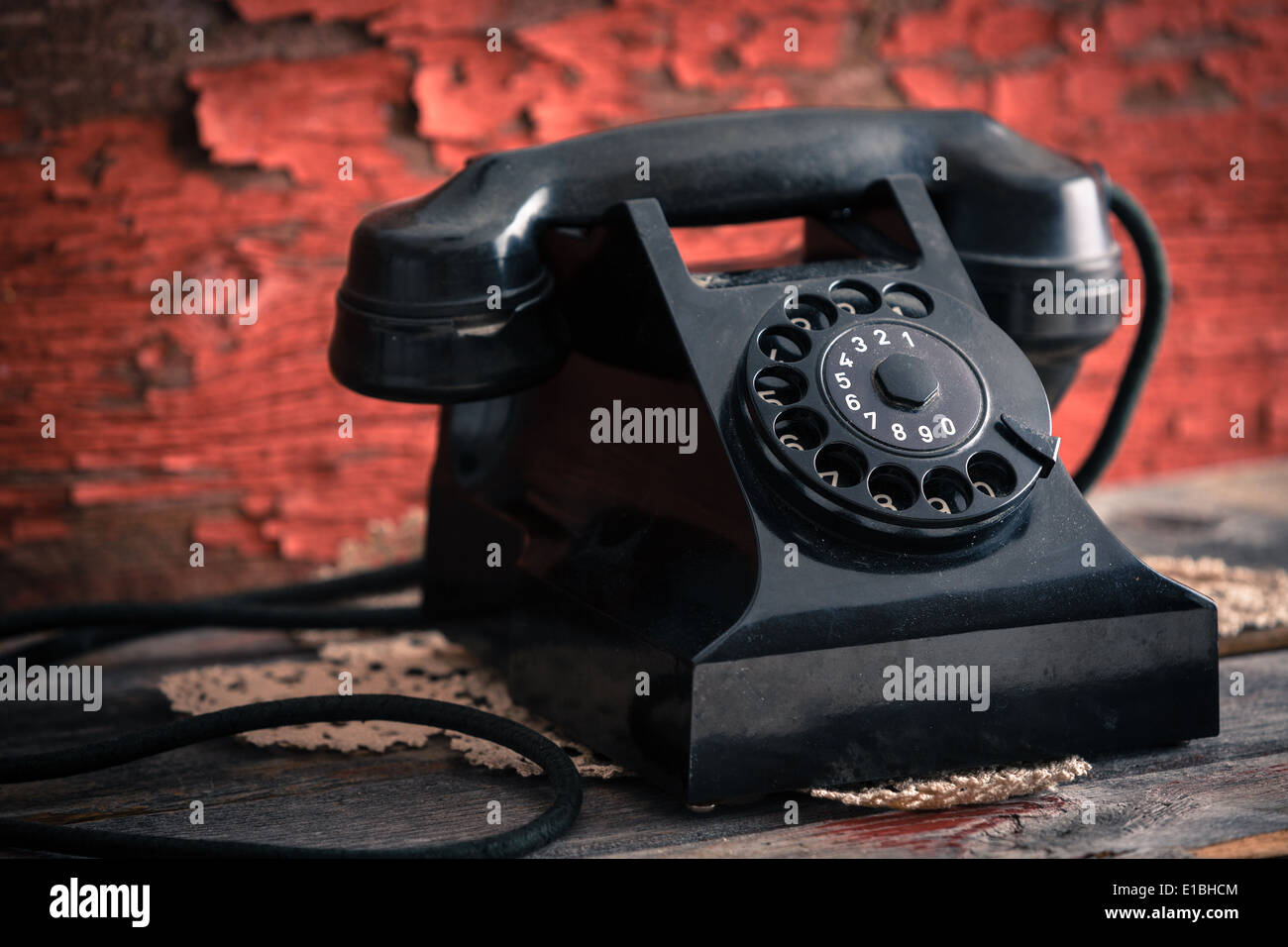 Close up side view of an old classic black dial-up rotary telephone against a grunge wooden wall with peeling red paint Stock Photo