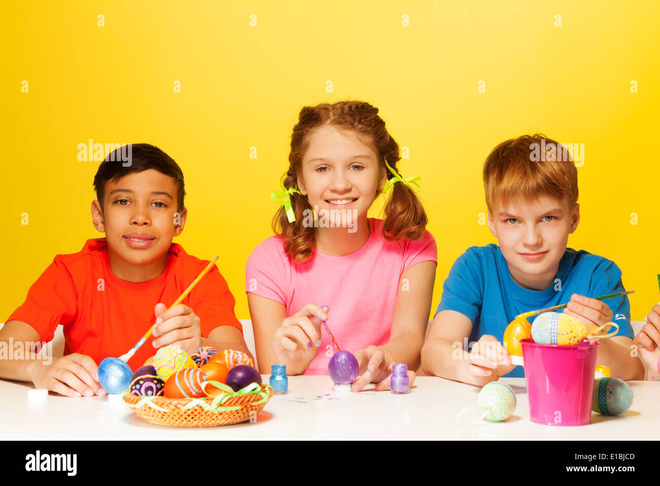 Two boys and girl paint Easter eggs at the table Stock Photo