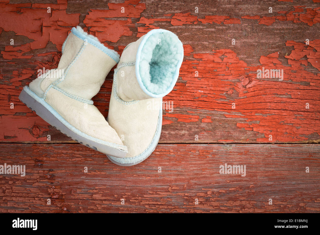 Pair of cozy warm winter sheepskin slippers lined with fluffy woolly fleece lying one upright and one on its side on rustic bg Stock Photo