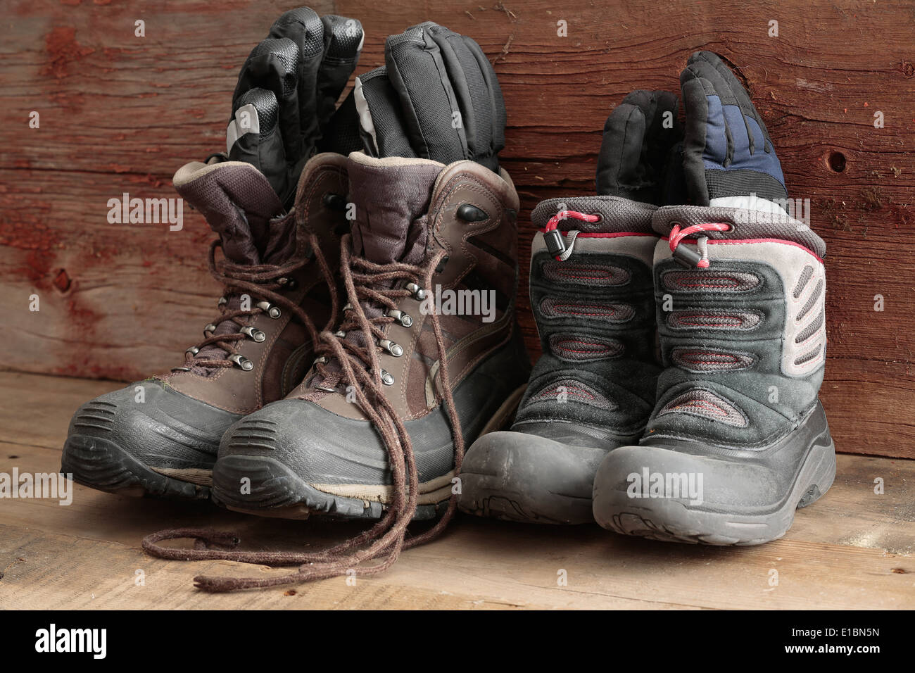 Adult and kids old winter snow boots with gloves inside them standing ready in a rustic wooden cabin to be worn outdoors in the Stock Photo
