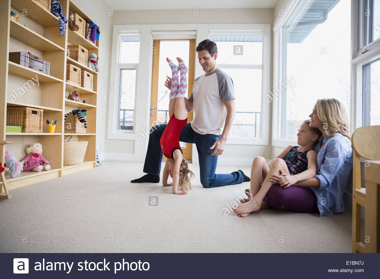 Father helping daughter do handstand in living room Stock Photo