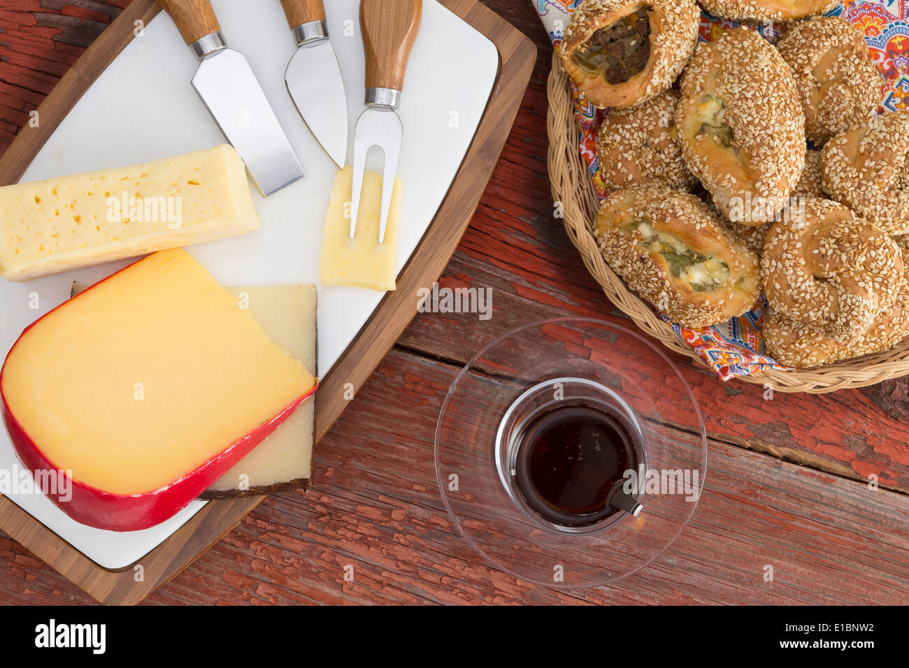 Serving of manchego,, gouda and havarti cheese on a cheeseboard with cutters and a glass of red wine alongside a basket of delic Stock Photo