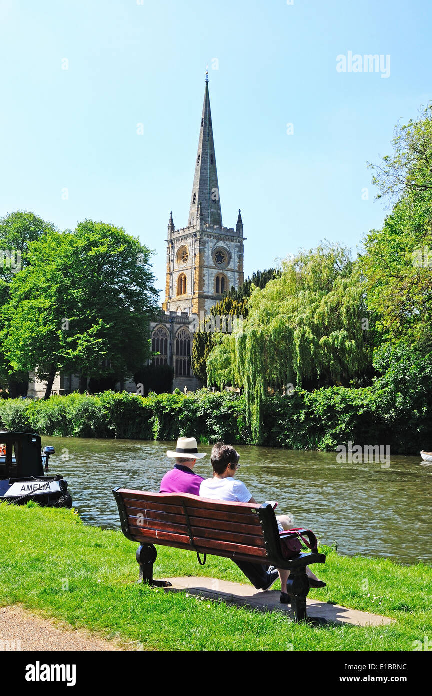 Holy Trinity Church seen across the River Avon with a couple sitting on a bench in the foreground, Stratford-Upon-Avon, UK. Stock Photo