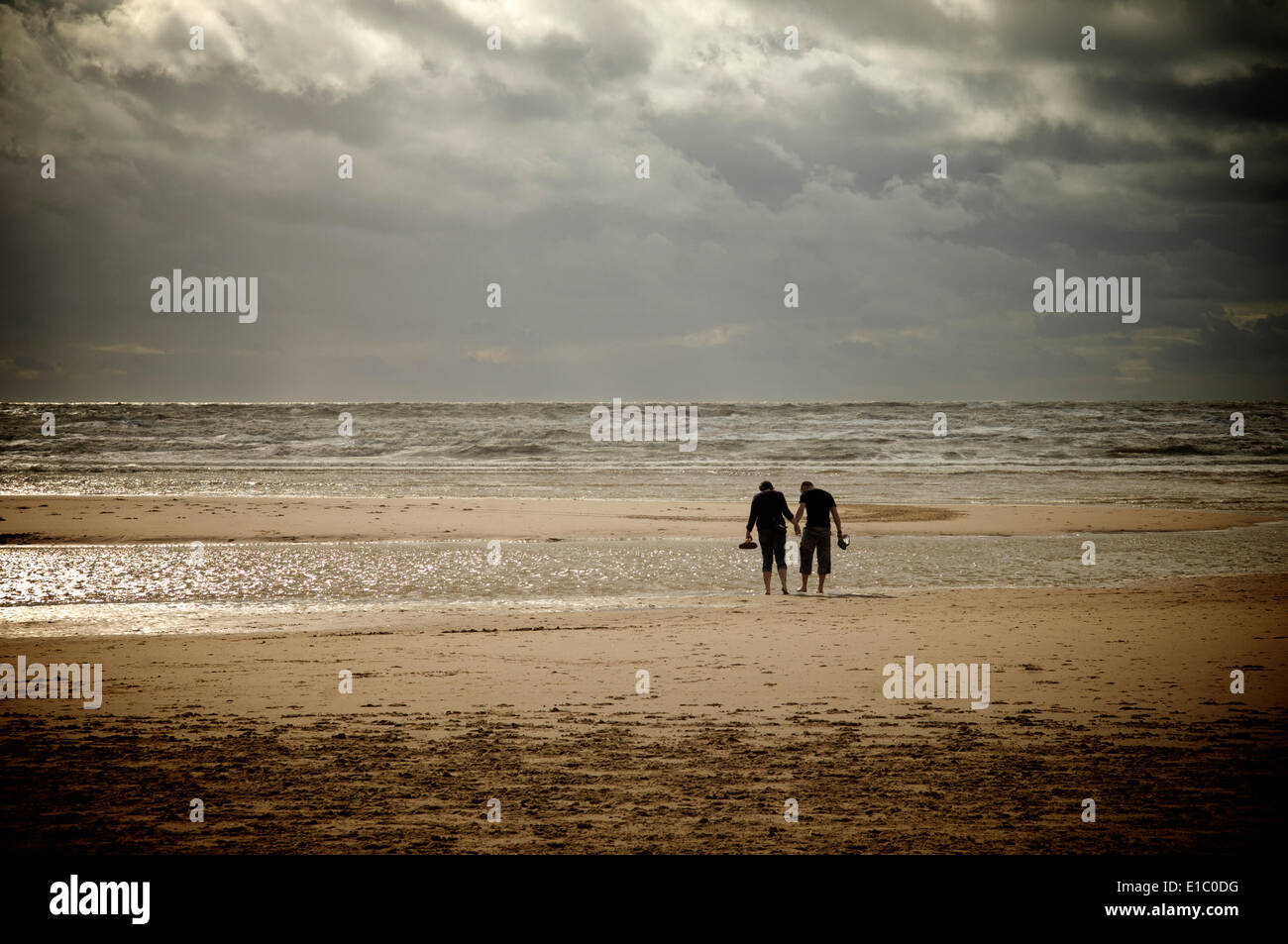 Couple padding on beach facing dramatic sky and sea Stock Photo