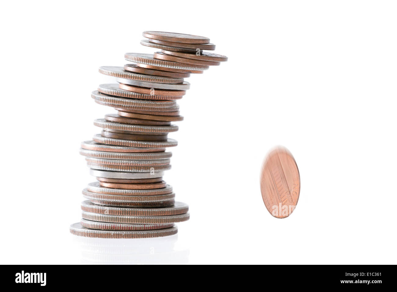 Precarious stack of coins of different denominations leaning to the side and falling over with one coin rolling away with motion Stock Photo
