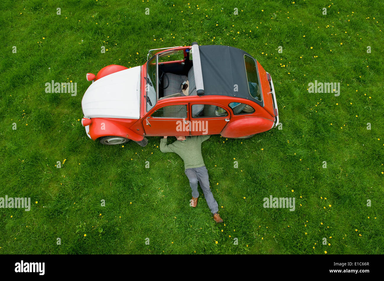 A man lying on his back under a red car, inspecting the underside of the car. Stock Photo