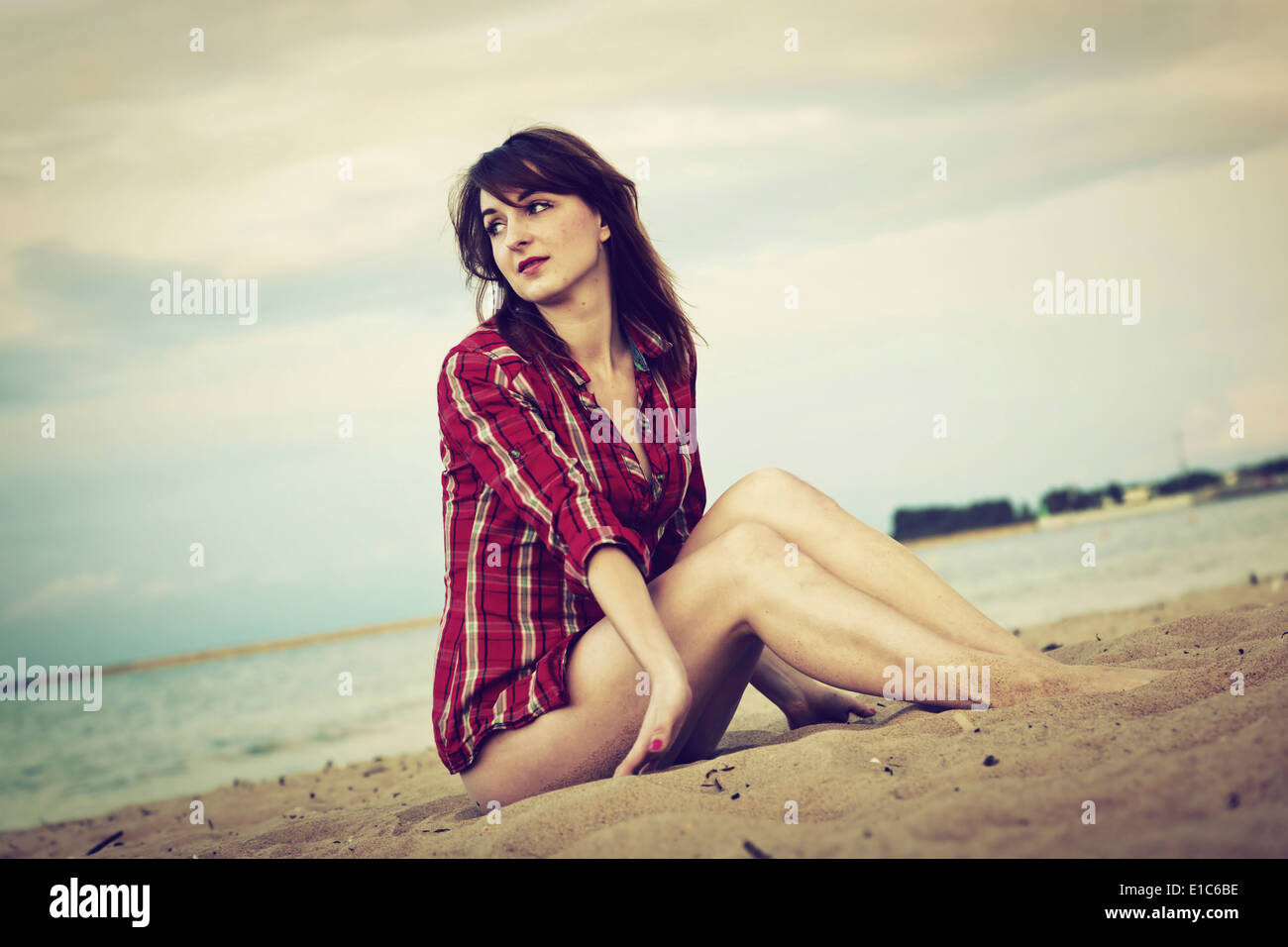 Young woman in a red checked shirt relaxing on the beach at sunset Stock Photo